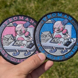 May include: Two embroidered patches featuring a cartoon character with glasses and a pink and blue background. The text on the patches reads "Yeoman, US Coast Guard".