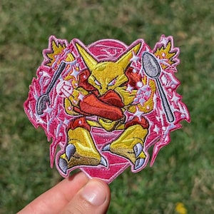 May include: An embroidered patch featuring a yellow creature with pointed ears and red armor accents, holding two silver spoons. The design is set against a vibrant pink circular background with white starbursts and jagged pink lightning bolt edges.