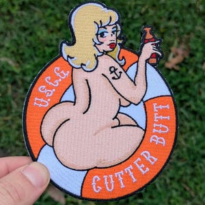 May include: Embroidered patch featuring a cartoon pin-up girl with blonde hair, holding a bottle. The design includes a life preserver with the text "Gutter Butt" and "U.S.C.G.". The patch is circular with orange, white, and blue colors.