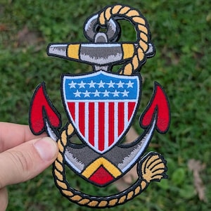 May include: Embroidered patch featuring a navy anchor design with a shield displaying red and white stripes and blue stars. The anchor has red accents and is surrounded by a yellow rope.