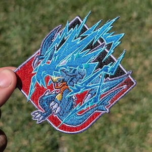 May include: A diamond-shaped embroidered patch featuring a blue creature with sharp claws and an orange neck accent, surrounded by bright blue lightning bolt patterns against a red and black background with a thick purple border trim.