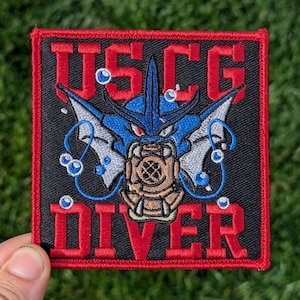Op de afbeelding: Een zwarte geborduurde patch met rode stiksels. De patch toont een blauwe en witte duiker met een duikhelm en de tekst "USCG DIVER" in rood.