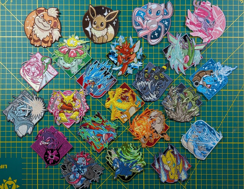 Puede incluir: Una colecci&oacute;n de veintid&oacute;s parches bordados que presentan varias criaturas de dibujos animados coloridas en poses din&aacute;micas. Cada parche muestra un personaje &uacute;nico, incluyendo tipos de fuego, agua y ps&iacute;quicos, con costuras detalladas sobre una cuadr&iacute;cula verde.