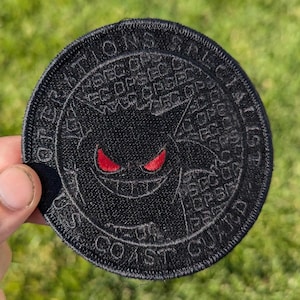 May include: Black embroidered patch with red eyes and the text "Operations Specialist US Coast Guard" around the edge.