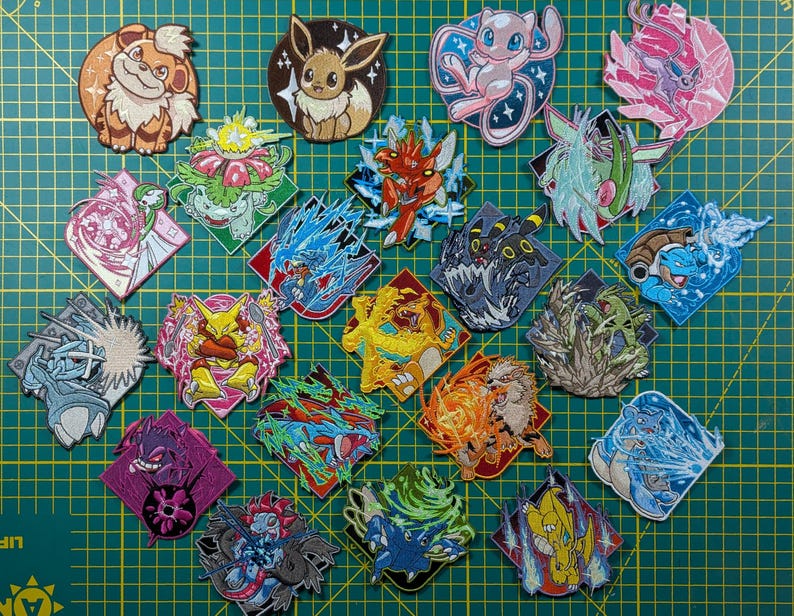 May include: A collection of twenty-two embroidered patches featuring various colorful cartoon creatures in dynamic poses. Each patch displays a unique character, including fire, water, and psychic types, rendered with detailed stitching on a green grid.