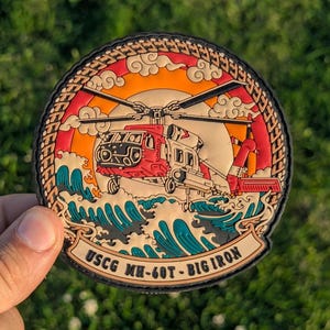 May include: A round patch featuring a red and white helicopter design, set against a vibrant sunset and ocean waves. The patch includes the text "USCG MH-60T - BIG IRON" in a banner, with a black border.