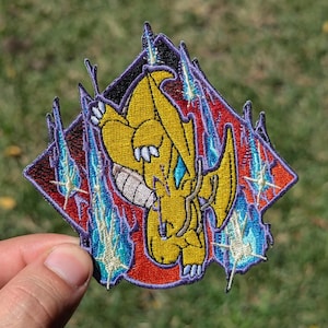 May include: A diamond-shaped embroidered patch featuring a yellow dragon-like creature in a dynamic pose. The design includes vibrant red and black background elements, accented by bright blue lightning bolts and white star-like sparkles.