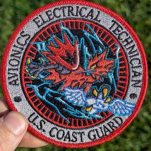 May include: Embroidered patch with a red, black, and blue design. The patch reads "AVIONICS ELECTRICAL TECHNICIAN" and "U.S. COAST GUARD" in a circular pattern. The central design features a stylized bird or dragon.