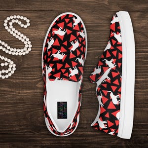 May include: A pair of slip-on shoes with a black background, red triangles, and white elephant silhouettes. The shoes have white soles and a white interior. The brand name "Giftables Galore!!" is printed on the insole.