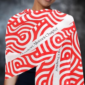 May include: A red and white patterned scarf with the text "Houston Alumni Chapter" in black. The scarf features a repeating design of concentric circles and lines. The scarf is draped over a person's shoulders.