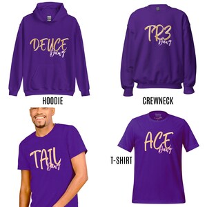 May include: A selection of purple clothing items: a hoodie, crewneck sweatshirt, and t-shirt, each with gold script lettering. The hoodie says "DEUCE Dawg", the crewneck reads "TR3 Dawg", and the t-shirt says "ACE Dawg". The fourth image shows a person wearing a purple t-shirt with "TAIL Dawg".