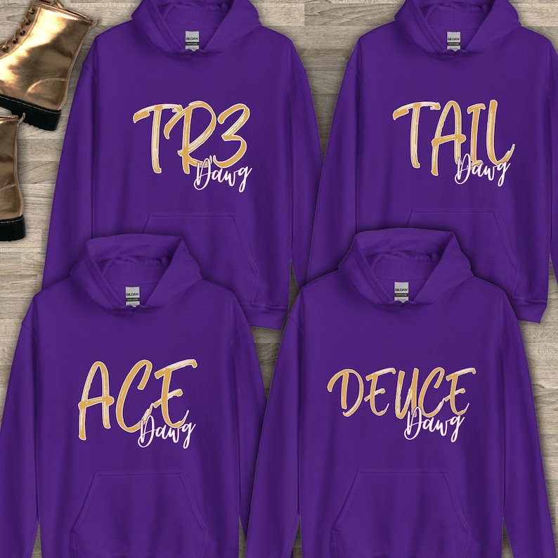 Puede incluir: Cuatro sudaderas con capucha moradas con letras doradas. Cada sudadera tiene un dise&ntilde;o diferente: "TR3 Dawg", "TAIL Dawg", "ACE Dawg" y "DEUCE Dawg". Las sudaderas tienen una capucha con cord&oacute;n y un bolsillo delantero.