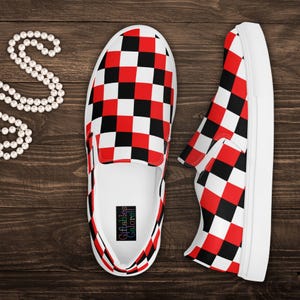 May include: Pair of slip-on shoes with a red, black, and white checkerboard pattern. The shoes have white soles and a white interior. The brand name "Giftables Galore!!" is printed on the insole. The shoes are displayed on a wooden surface.