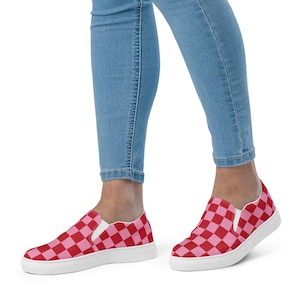 Op de afbeelding: Instappers met een rood en roze dambordpatroon. De schoenen hebben een witte zool en worden gedragen met een blauwe spijkerbroek. De sneakers zijn een casual stijl, geschikt voor dagelijks gebruik.