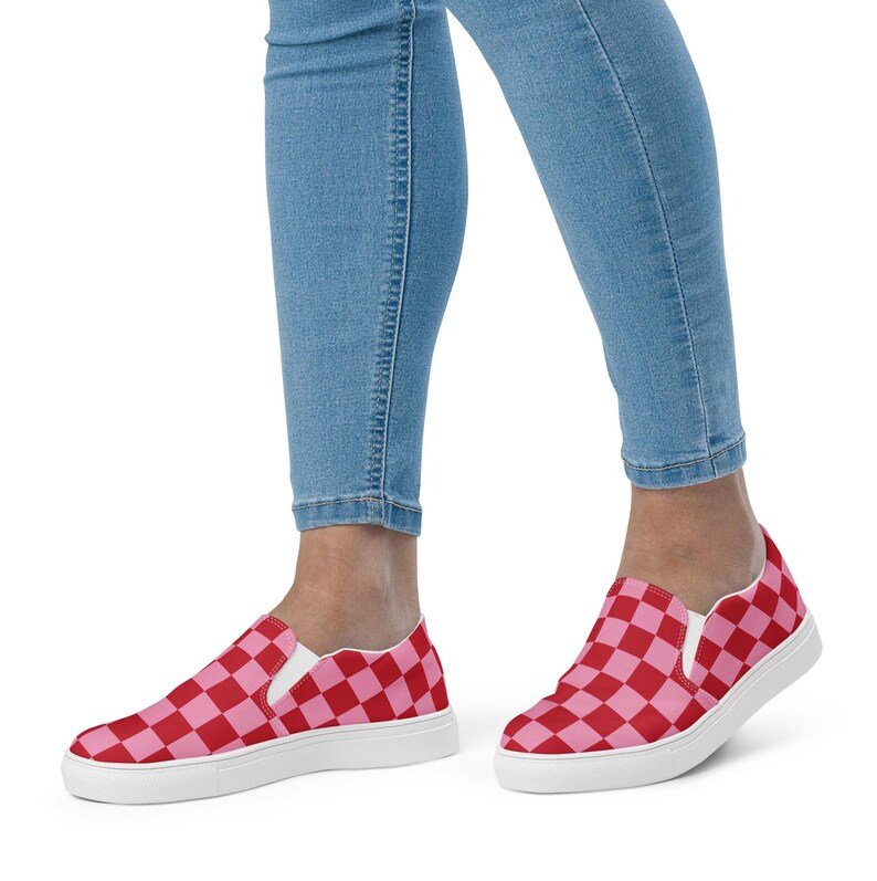 Op de afbeelding: Instappers met een rood en roze dambordpatroon. De schoenen hebben een witte zool en worden gedragen met een blauwe spijkerbroek. De sneakers zijn een casual stijl, geschikt voor dagelijks gebruik.