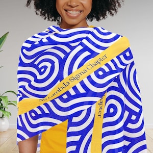 May include: A blue and white patterned scarf with a repeating swirl design. The scarf has a yellow band with the text "Nu Lambda Sigma Chapter". The scarf is draped over a yellow top.