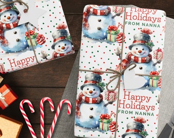 Op de afbeelding: Wit inpakpapier met een rood en groen stippenpatroon. Het papier heeft een aquarel-illustratie van sneeuwpoppen met rode sjaals en hoeden. De tekst "Happy Holidays from Nanna" is op het papier gedrukt.