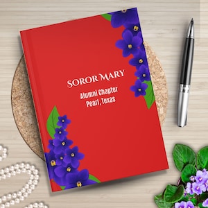 May include: Red notebook with the text "SOROR MARY Alumni Chapter Pearl, Texas" and purple flowers on the cover.
