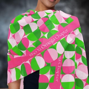 May include: A vibrant scarf with a geometric pattern of green, pink, and white semi-circles. The scarf has a pink band with the text "Rho Xi Omega Chapter". The scarf is draped over a person's shoulders.