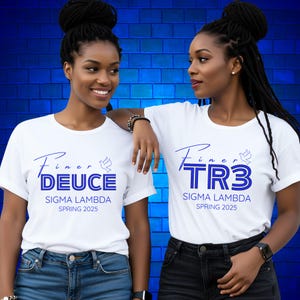 May include: Two women wearing white t-shirts with blue text. The shirts say "Finer DEUCE" and "Finer TR3" with "Sigma Lambda Spring 2025" below. They are standing in front of a blue brick wall.