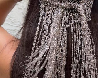 Könnte beinhalten: Ein silbernes Kopfstück mit netzartigem Design, verziert mit schimmernden Pailletten. Lange, herabhängende Strähnen aus dem gleichen Material fallen kaskadenartig herab und erzeugen einen fließenden, eleganten Effekt. Das Kopfstück ist zum Tragen auf dem Kopf bestimmt.