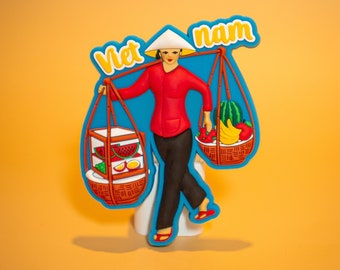 May include: A blue and white souvenir magnet featuring a woman carrying two baskets of fruit. The text "Viet nam" is written in yellow across the top of the magnet.