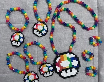 May include: A set of rainbow-colored beaded bracelets and necklaces with mushroom charms. The charms are pixelated and feature a rainbow design.