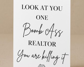 May include: A white greeting card with black text that reads "LOOK AT YOU ONE Bomb Ass REALTOR You are killing it." A small house illustration is at the bottom. The card is folded.