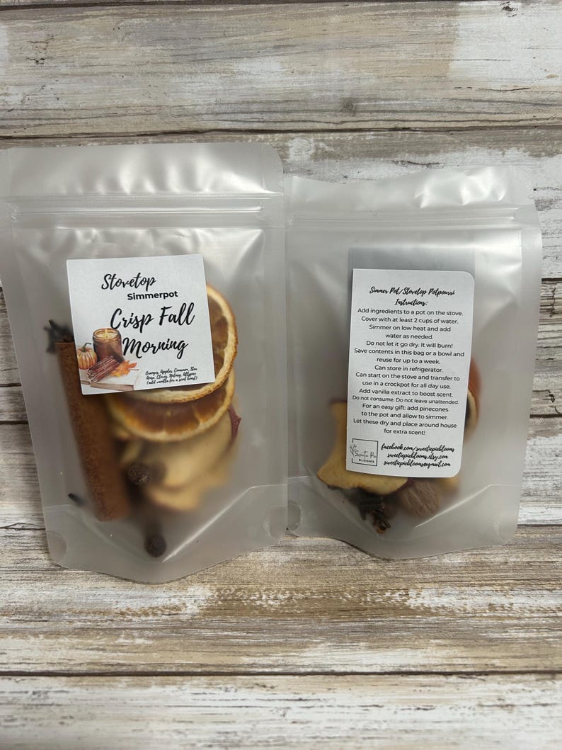May include: Two clear plastic bags containing ingredients for a stovetop simmer pot. One bag features dried orange slices, cinnamon sticks, and other spices. The label reads "Stovetop Simmerpot Crisp Fall Morning."