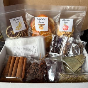 May include: A white box filled with various ingredients for crafting. Includes bags of dehydrated lemons, oranges, and apples, along with cinnamon sticks, star anise, and other spices. The bags have labels with the product names.