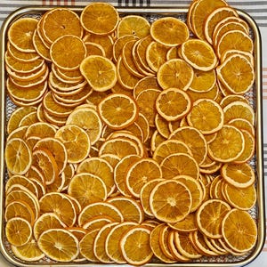 Pode incluir: Um tabuleiro retangular de metal cheio de uma grande quantidade de fatias de laranja desidratadas cortadas finamente. As fatias s&atilde;o de cor laranja dourada, mostram a estrutura da polpa e a casca, dispostas numa camada densa e sobreposta.