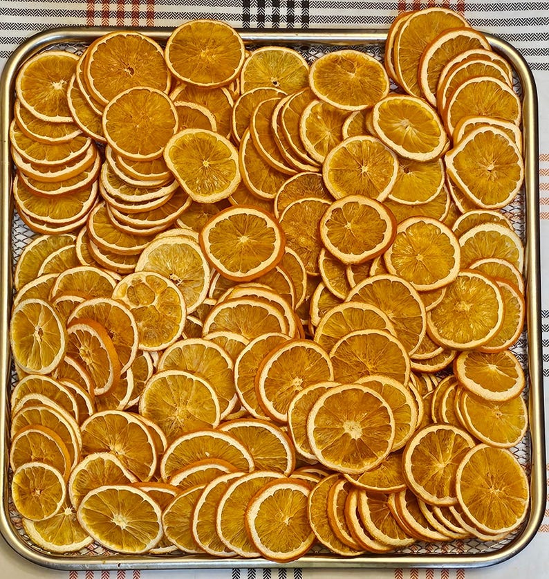 Pode incluir: Um tabuleiro retangular de metal cheio de uma grande quantidade de fatias de laranja desidratadas cortadas finamente. As fatias s&atilde;o de cor laranja dourada, mostram a estrutura da polpa e a casca, dispostas numa camada densa e sobreposta.