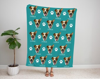 May include: A teal blue fleece blanket with a repeating pattern of a dog's face and white paw prints. The dog's name, "Charlie", is printed below each face.