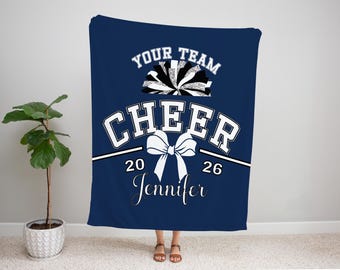 May include: Navy blue blanket with the text "YOUR TEAM CHEER 2026 Jennifer" in white. The blanket features a pom-pom graphic and a bow graphic. The blanket is displayed in a room with a plant.