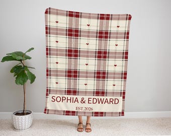 May include: A red, cream, and dark red plaid blanket with small red heart accents. The blanket has a cream-colored banner at the bottom with the names "SOPHIA & EDWARD" and the year "EST.2026" in dark red text.