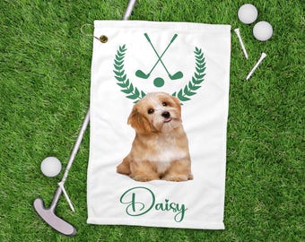 May include: White golf towel with a green golf club and wreath design, and a cute dog illustration. The name "Daisy" is written in green script below the dog. Golf balls, tees, and a putter are visible on the green grass.