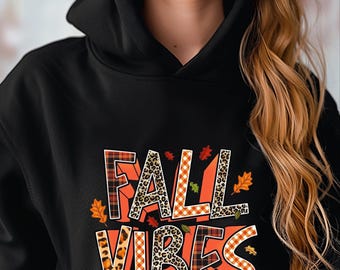 May include: Black hooded sweatshirt with the words "FALL VIBES" in a colorful, fall-themed design. The text incorporates leopard print, plaid, and autumn leaf accents. The sweatshirt has a drawstring hood.
