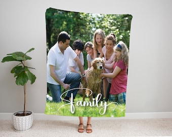 May include: A family of six, including a dog, stand in a grassy field. The dog is brown and white and is surrounded by the family. The family is smiling and looking at the camera. The text "family" is written in white cursive on the grass in front of the family.