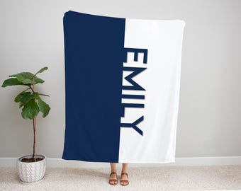 May include: A navy blue and white blanket with the name "EMILY" printed vertically in navy blue. The blanket is divided into two sections, with navy blue on the left and white on the right. The blanket is displayed indoors.