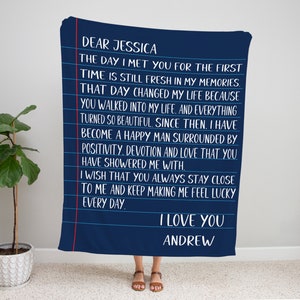 May include: A navy blue throw blanket with a handwritten message in white text on a white lined background. The message reads: "Dear Jessica, The day I met you for the first time is still fresh in my memories. That day changed my life because you walked into my life, and everything turned so beautiful. Since then, I have become a happy man surrounded by positivity, devotion and love that you have showered me with. I wish that you always stay close to me and keep making me feel lucky every day. I love you, Andrew."
