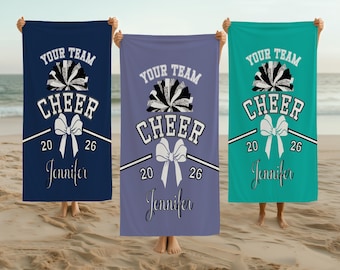 May include: Three beach towels in navy blue, lavender, and teal, each with the text "YOUR TEAM CHEER" and a bow design. The towels also feature the year "2026" and the name "Jennifer".