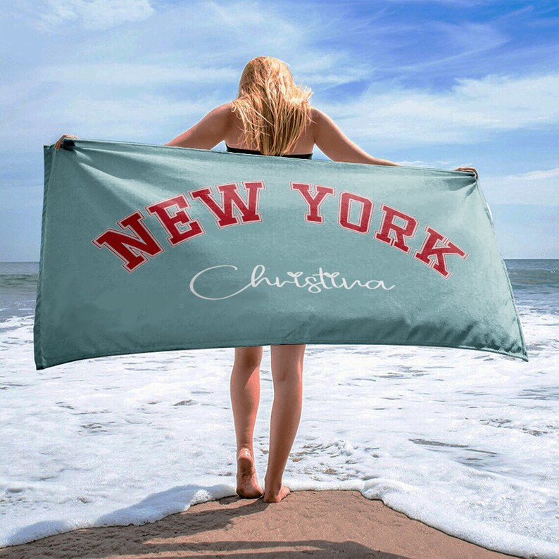 May include: A turquoise beach towel with the text "NEW YORK" in red and the name "Christina" in white cursive writing.