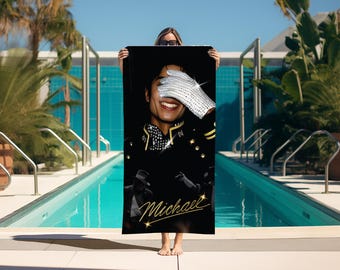 May include: A rectangular beach towel featuring a black background with a portrait of Michael Jackson wearing a sequined glove over his face. The design includes a black military-style jacket with gold accents and the name Michael in gold script.