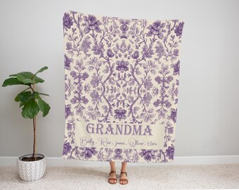 May include: A floral patterned blanket in shades of purple and cream. The blanket features a repeating design of flowers and foliage. The word "GRANDMA" is displayed in a banner, with names below. A decorative home textile.