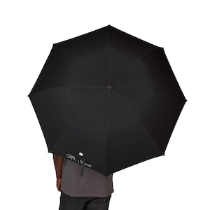 May include: A black umbrella, fully open, with a silver-colored handle. The umbrella's canopy is a solid black color. The text "Mr. Smith" is printed in a cursive font on the umbrella.