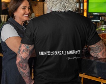 May include: A black t-shirt with the text "Kindness speaks all languages - The Universe" printed on the back. The shirt is being worn by a person with long, gray hair.