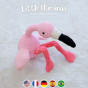 May include: A pink crocheted flamingo toy with a white and black beak. The toy is sitting on a white fluffy surface. The text "Little Flamingo Low-Sew Pattern" is above the toy.