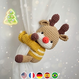 May include: A crocheted reindeer ornament in brown and white with a red nose, holding onto a white curtain. The reindeer is wearing a yellow and white striped sweater.