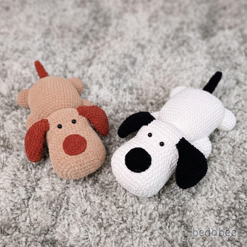 May include: Two handmade crochet dog toys. One is tan with rust-colored ears and a red nose. The other is white with black ears and a black nose. Both have black eyes and a tail.