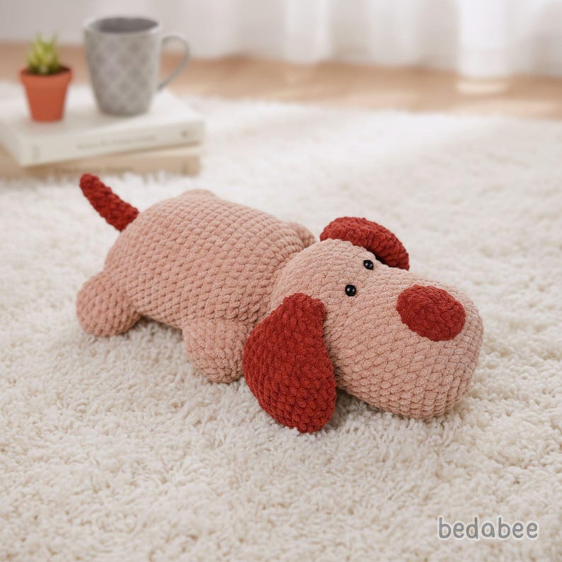 May include: A plush dog toy in a light pink color with dark red ears, nose, and tail. The dog is lying down on a white carpet. The toy has black button eyes and a textured surface.
